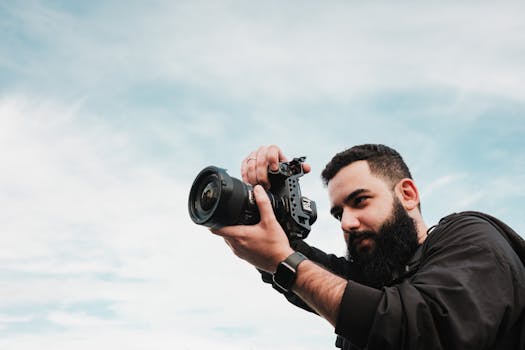 A bearded man focuses while taking a photo with a DSLR camera outdoors.