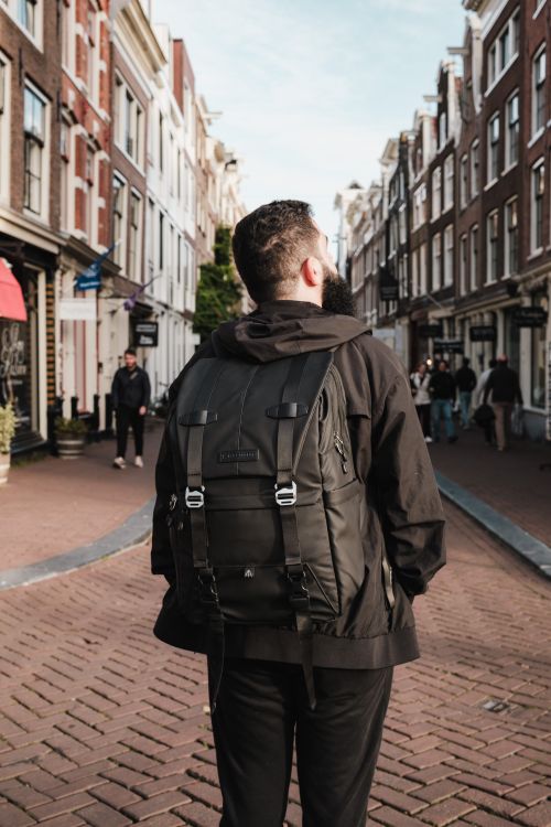 Free Man in black jacket exploring scenic Amsterdam street with historic buildings. Stock Photo