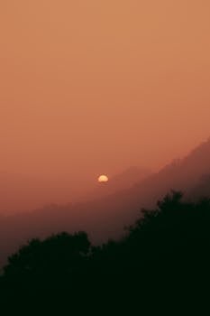 Sunrise over misty mountains with warm hues and dramatic sky.