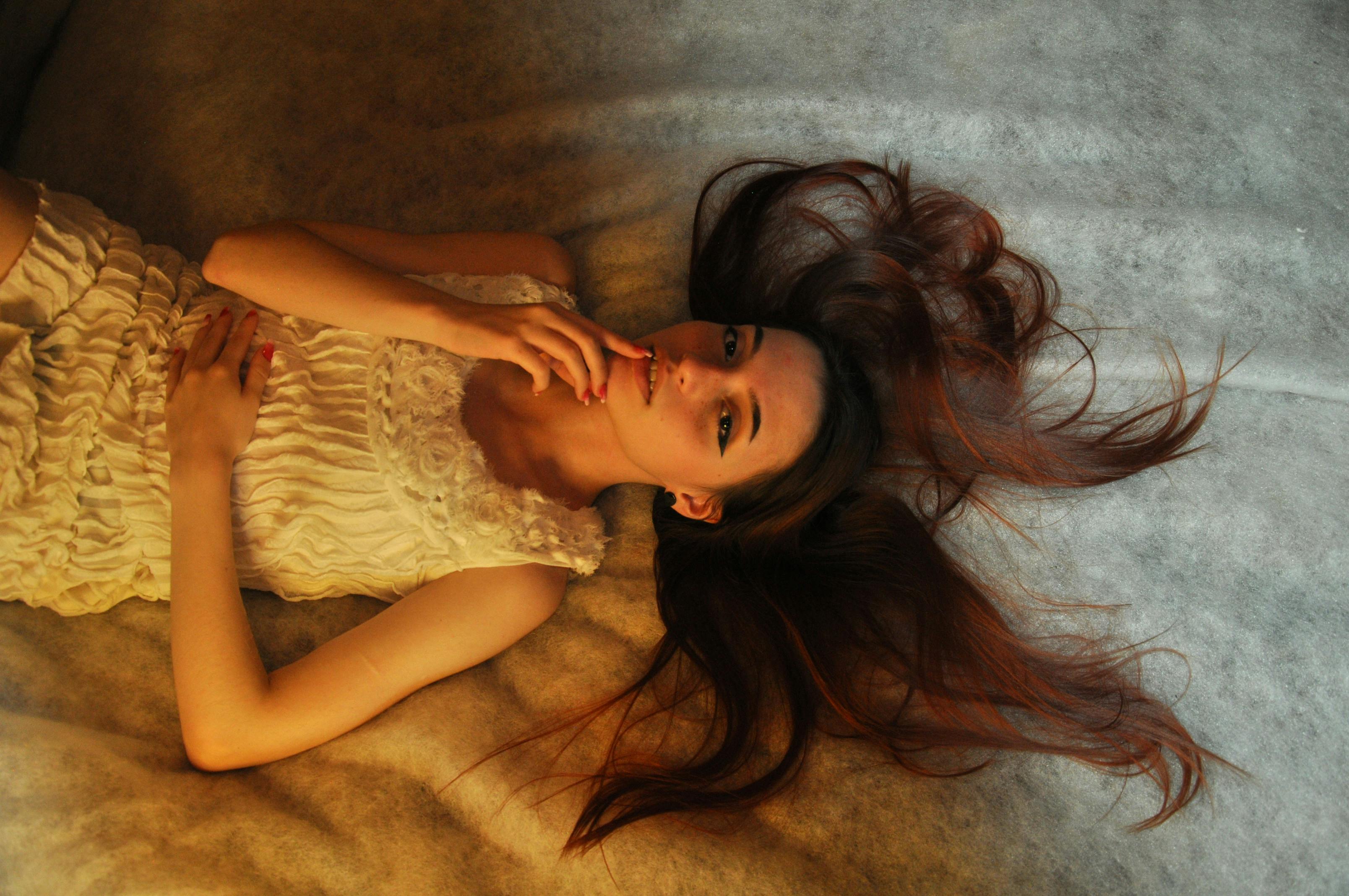 Candid portrait of a woman in a white dress reclining gracefully on a soft surface.