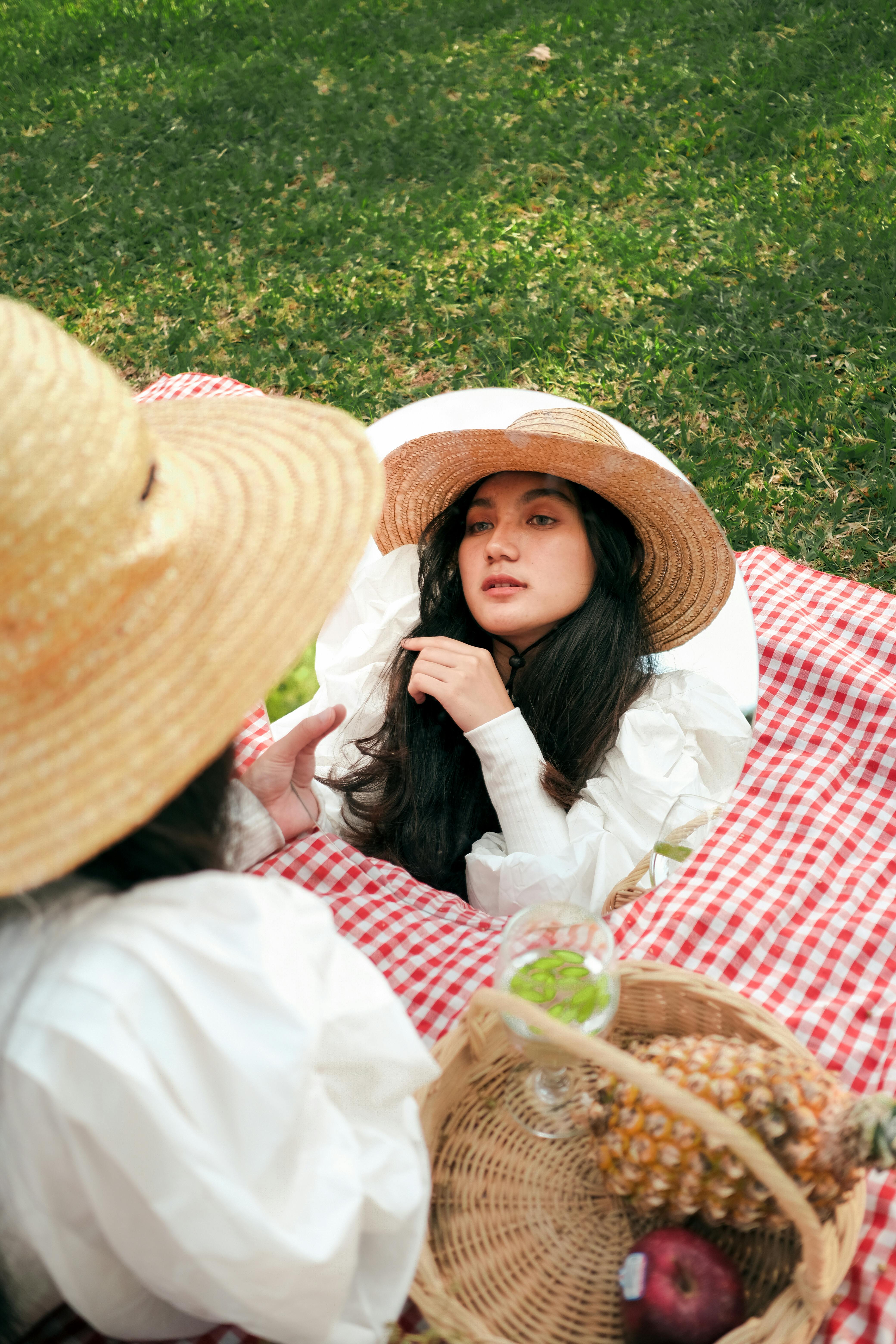 Young woman in a straw hat reflected in a mirror during a summer picnic outdoors.