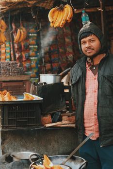 Man standing at a street vendor stall in a bustling urban market, surrounded by fresh produce.