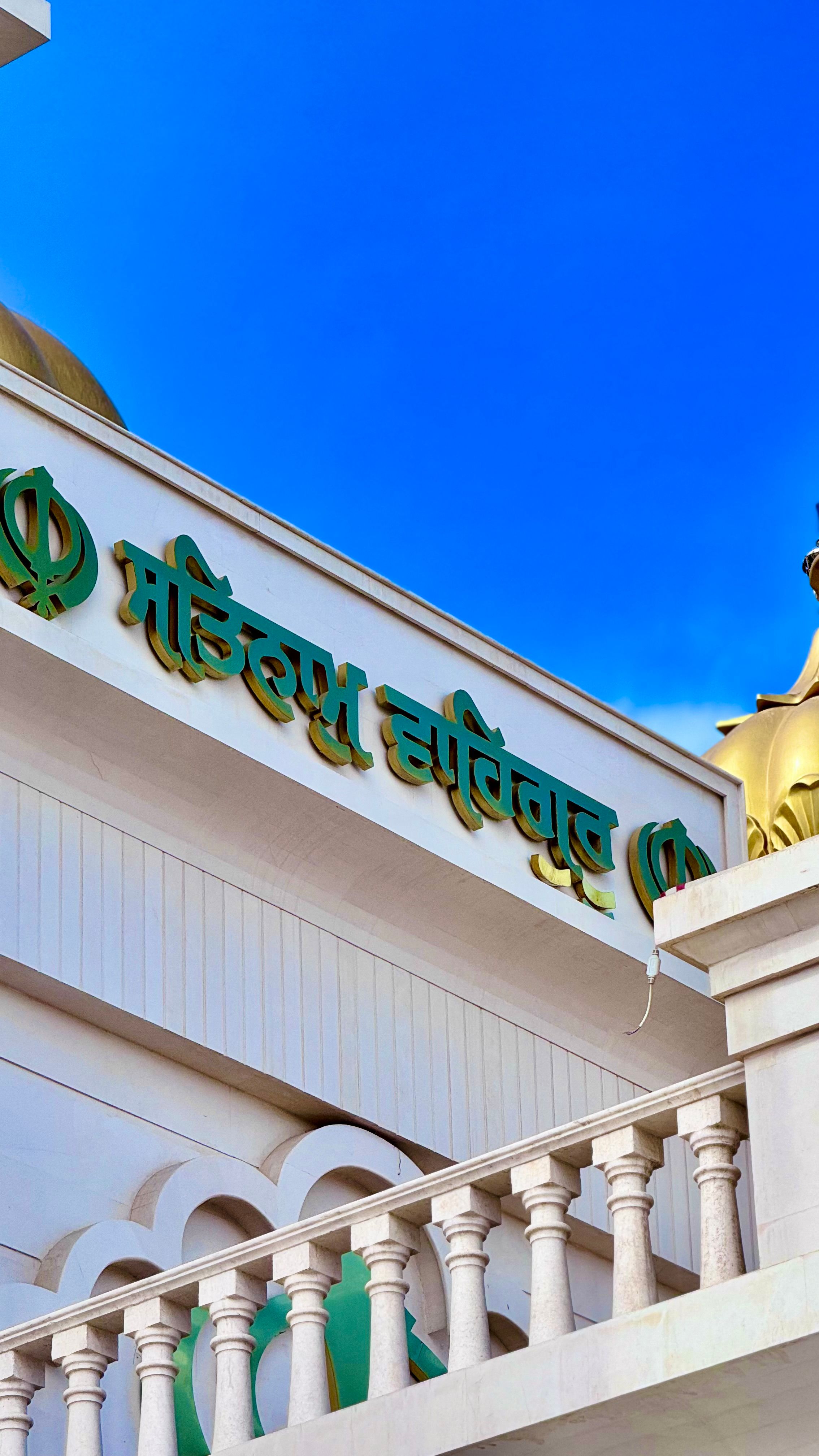 Close-up of Sikh temple facade with text and railings under a clear blue sky.