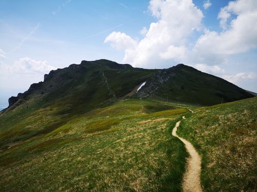 Free A scenic footpath winds through a vibrant green mountain landscape under a bright spring sky. Stock Photo