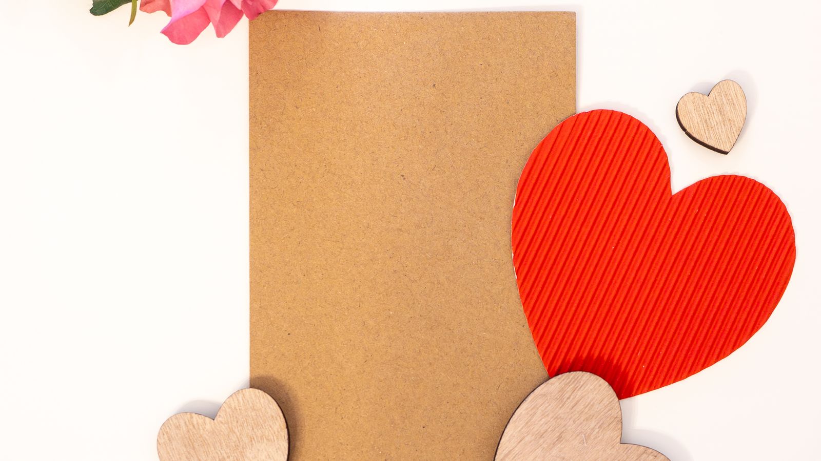 A blank brown card beside a pink rose and heart-shaped decorations