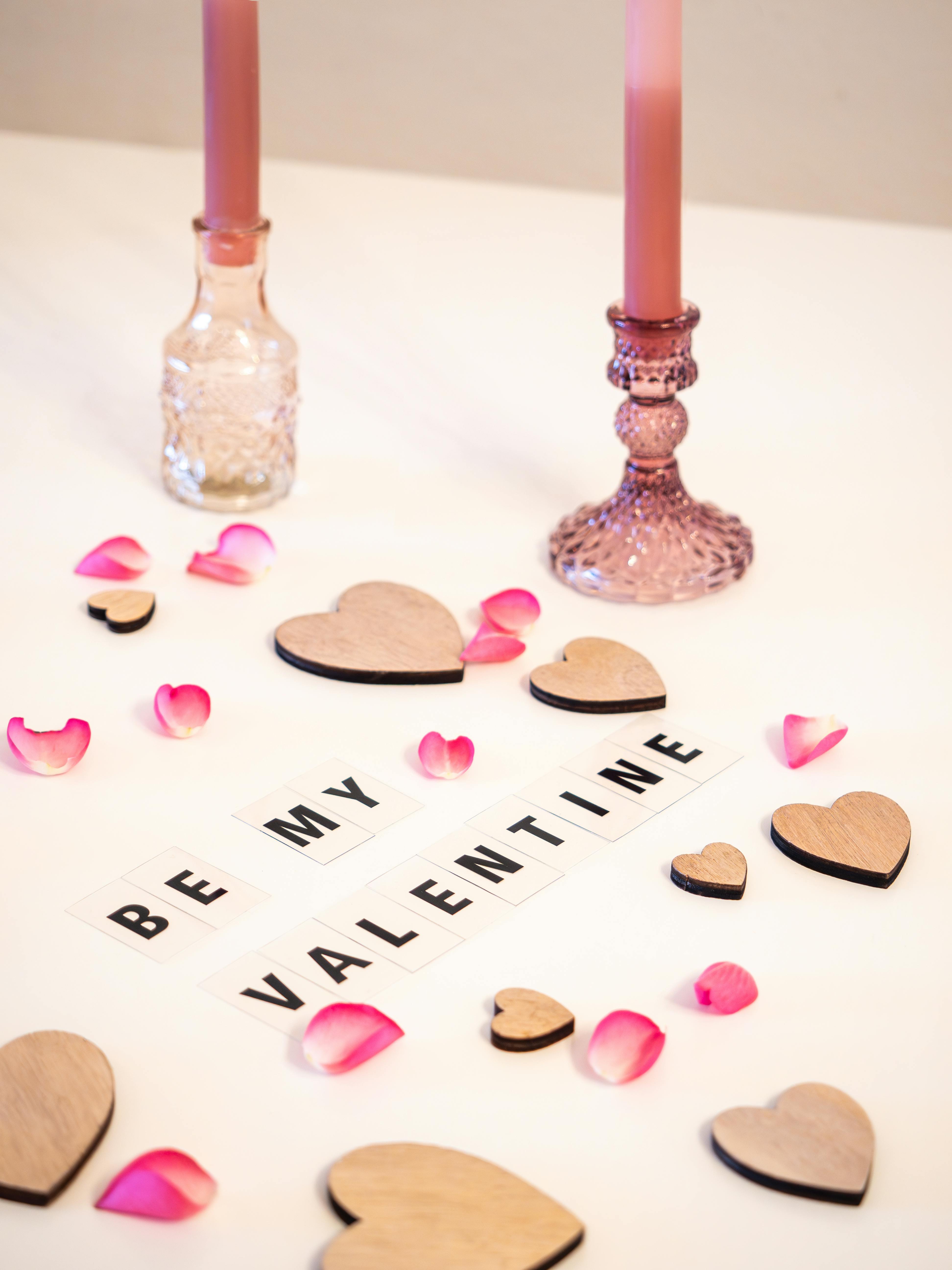 Delicate Valentine's Day arrangement with candles, hearts, and rose petals on a white background.