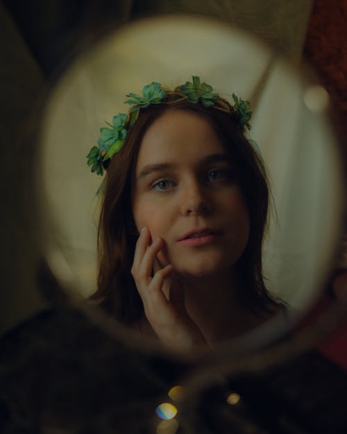 Young Woman Wearing a Green Headdress Looking at Herself in a Round Mirror