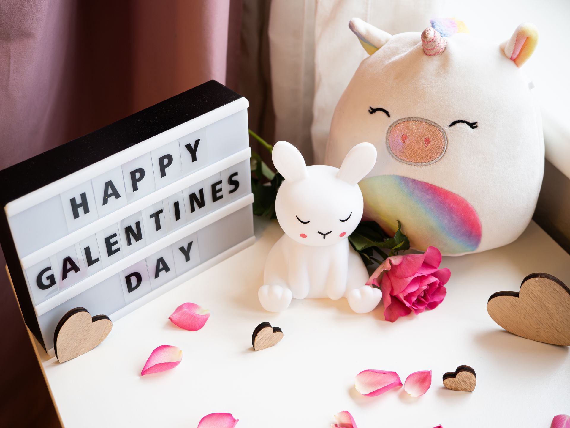 Cute Galentine's Day setup with plush unicorn, bunny figurine, rose petals, and message board.