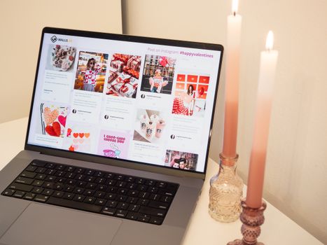 A romantic setup featuring a laptop with Valentine's posts and pink candles, perfect for a cozy atmosphere.