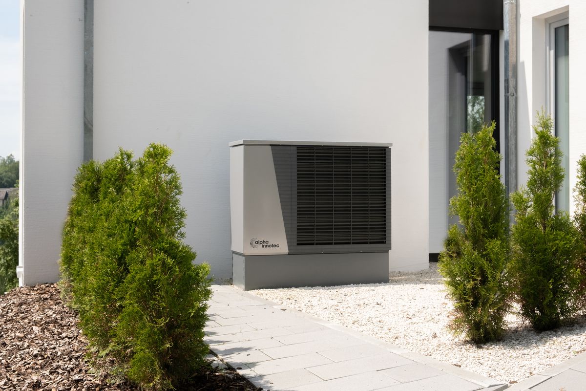 Unité extérieure de pompe à chaleur sur une maison moderne, entourée de verdure