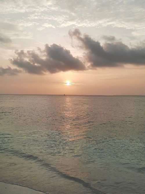 Free A tranquil sunset over the serene waters of Zanzibar, Tanzania, with a sailboat on the horizon. Stock Photo