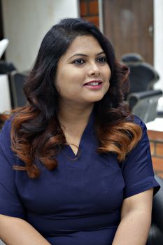 Portrait of a smiling woman with long, curly hair sitting in a salon chair.