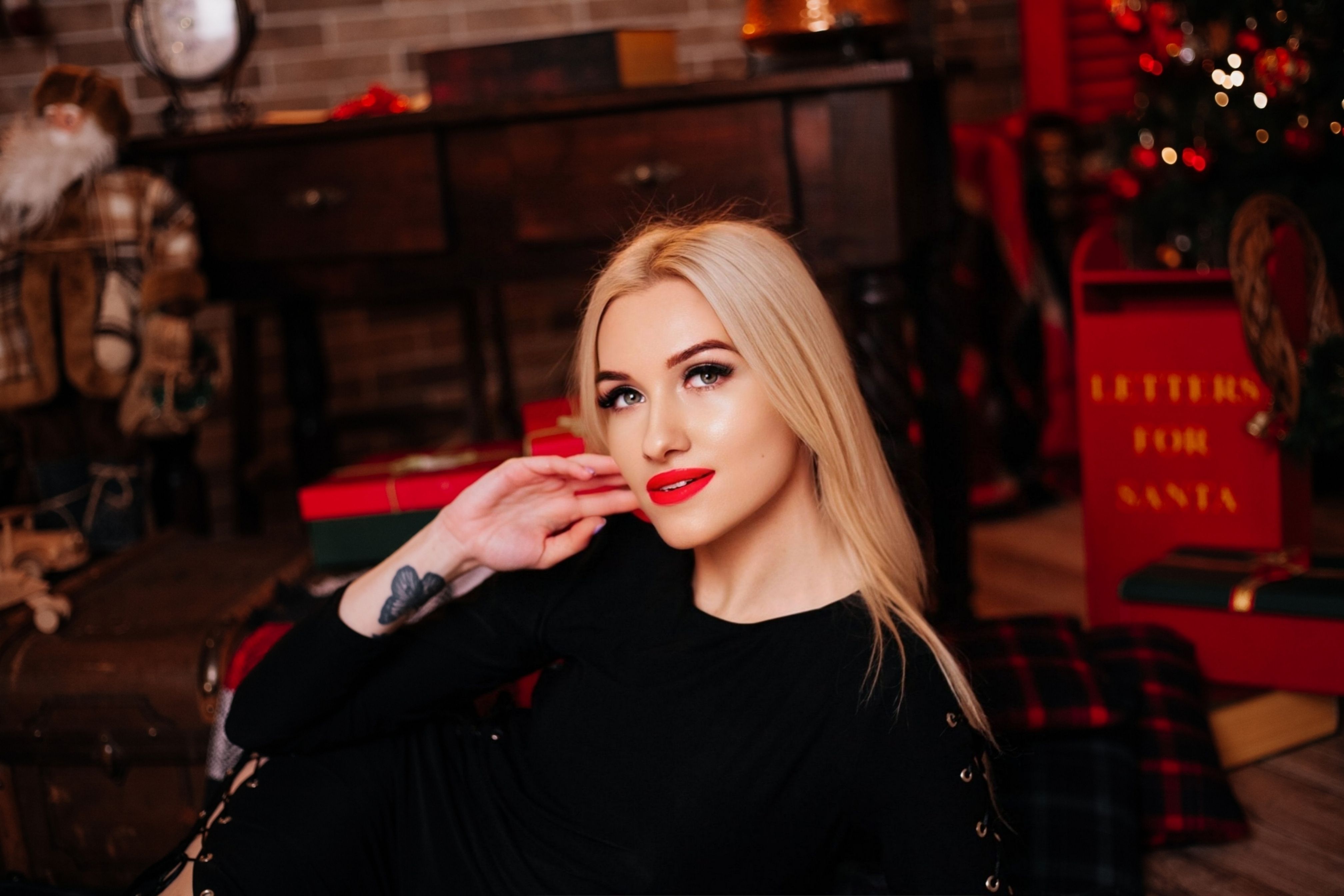 Blonde woman indoors with Christmas decor, gifts, and festive ambiance.