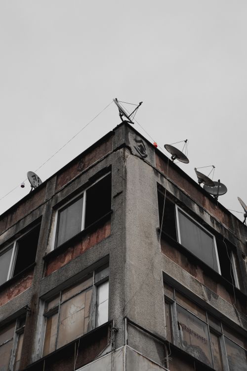 Free An aged, urban building featuring satellite dishes on a cloudy day, capturing urban decay. Stock Photo