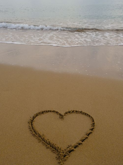 Free A heart drawn in the sand at a serene beach with gentle waves lapping the shore. Stock Photo