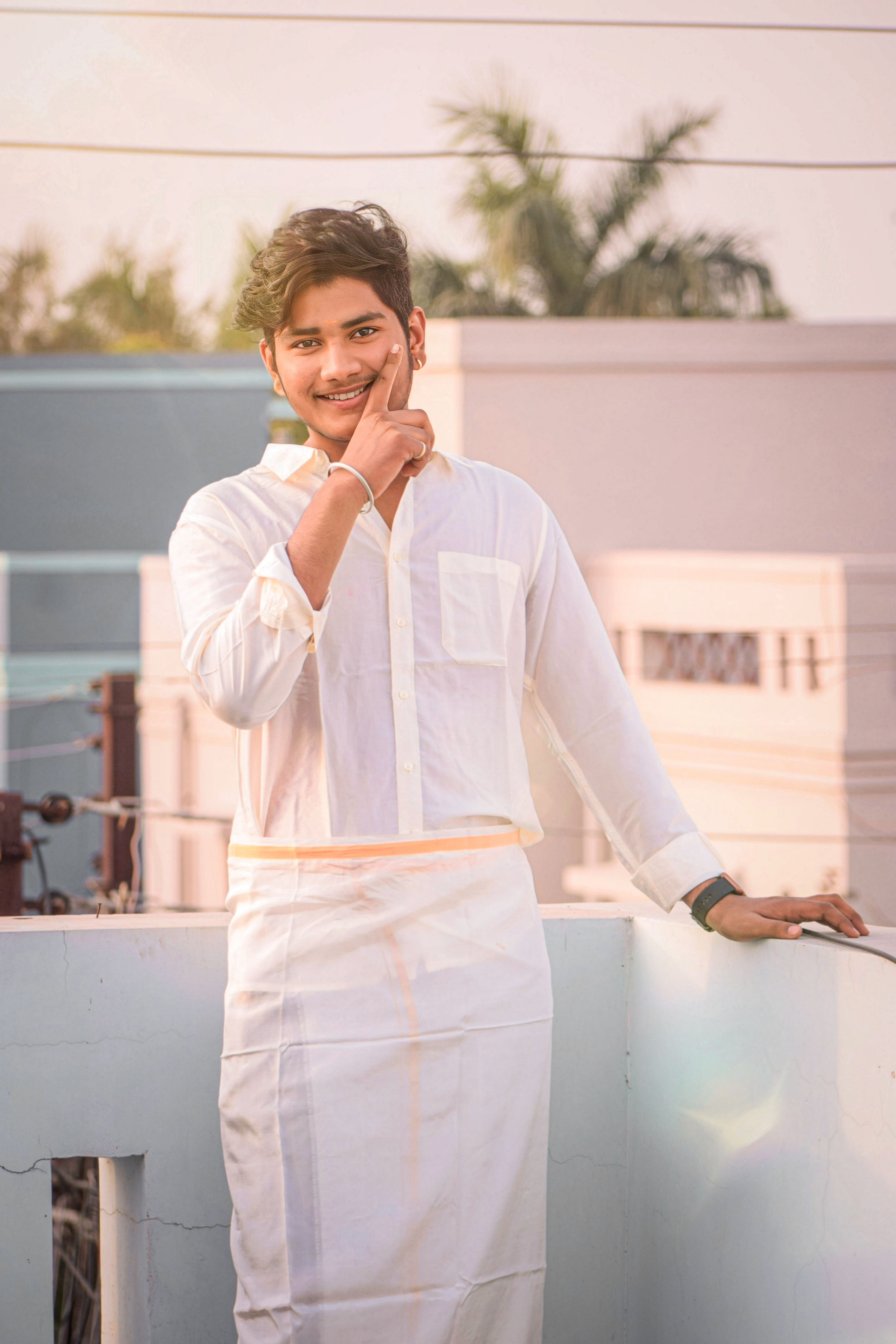 A young man smiles on a terrace in traditional attire, enjoying the sunny day.