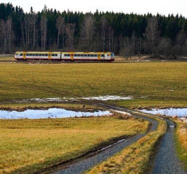A scenic view of a passenger train traveling through a rural meadow with snow patches.