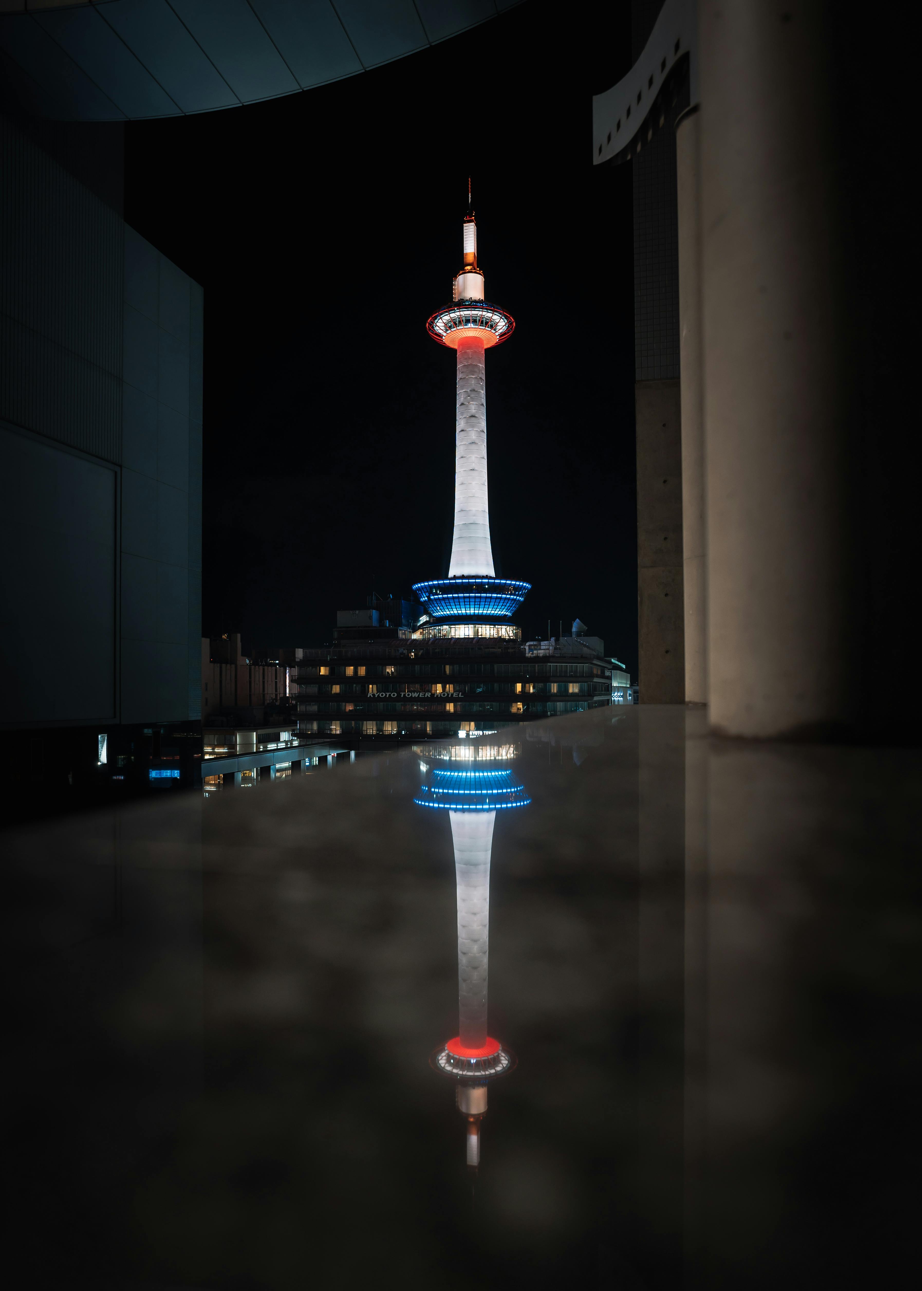 Dazzling view of illuminated Kyoto Tower reflected on a surface at night in Kyoto, Japan. A stunning urban landmark.