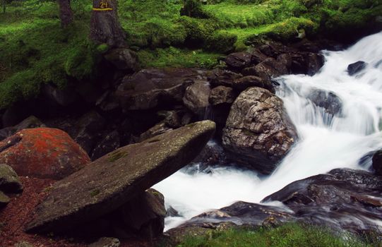Flowing water stream in lush forest with moss-covered rocks in Vipiteno, Italy.
