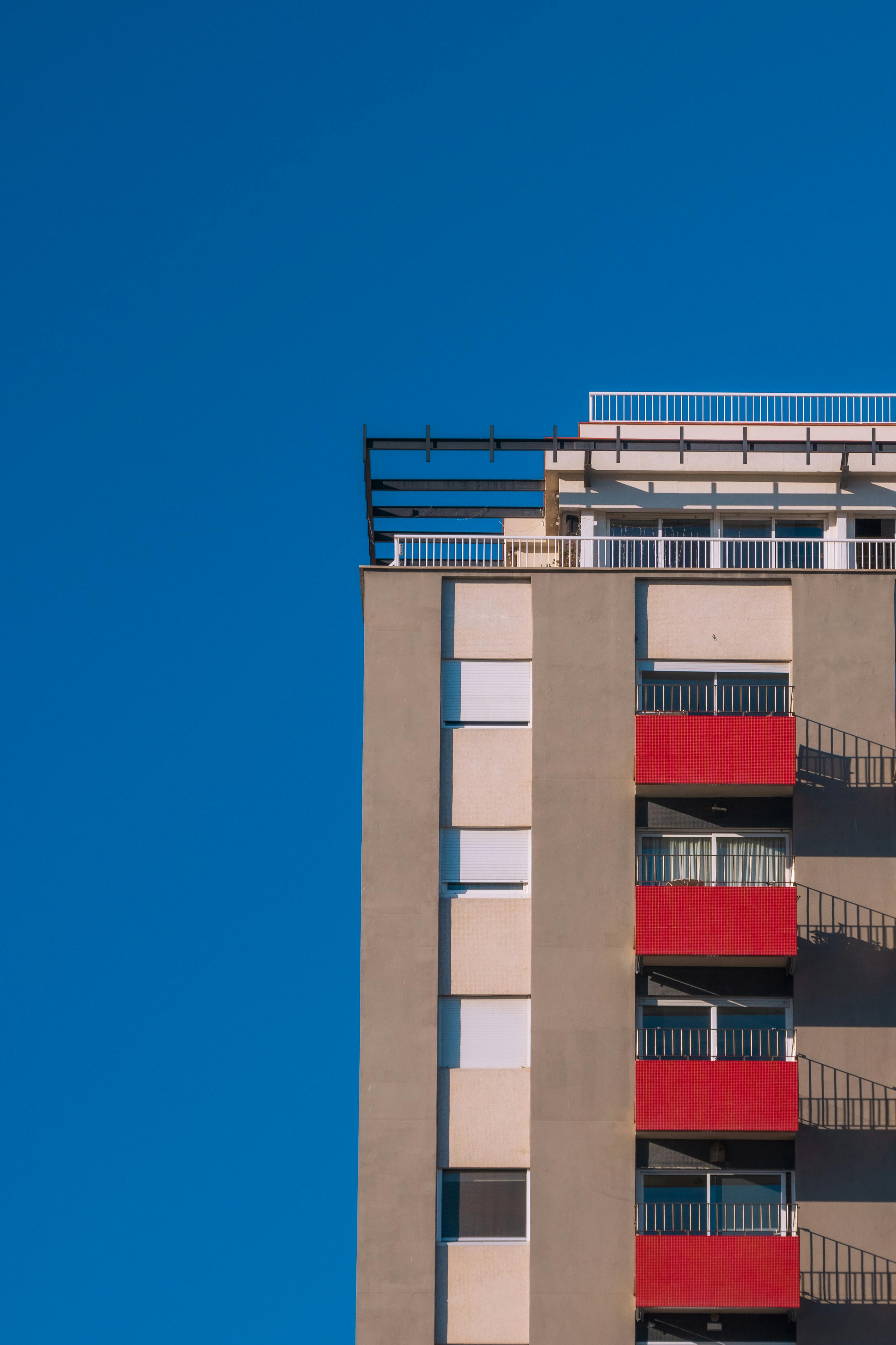 Side view of a tall residential building with red balconies against a blue sky.