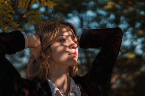 Free A young Caucasian woman posing outdoors under dappled sunlight in a serene, natural setting. Stock Photo