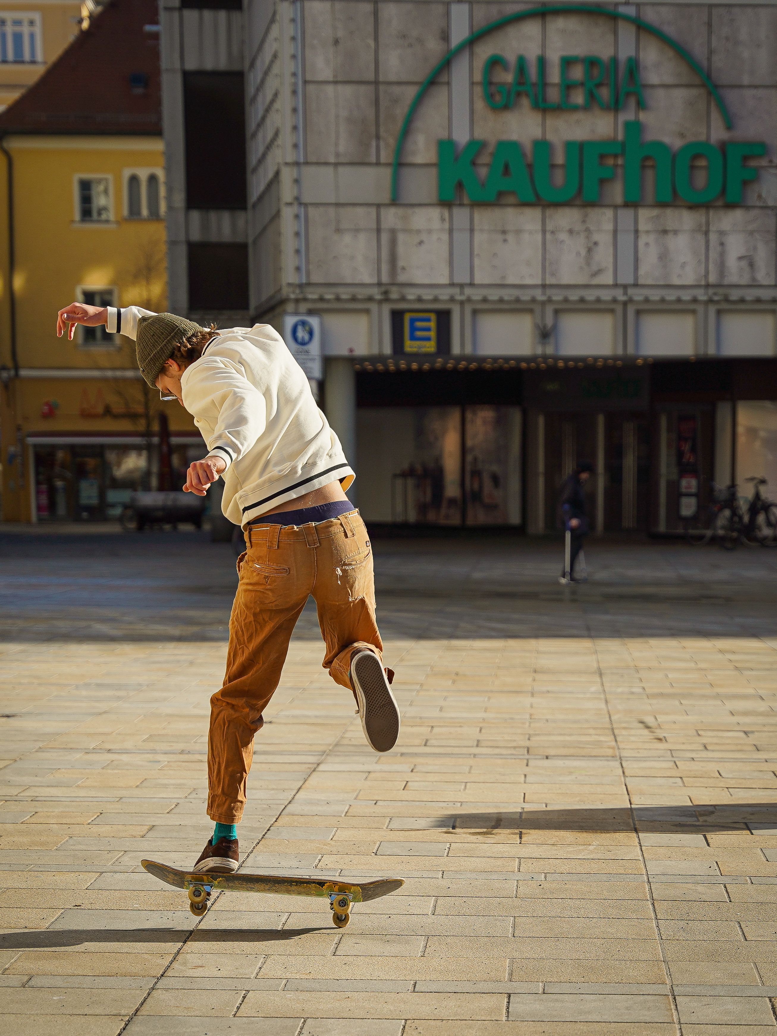 A skateboarder showing his skills in front of Galeria Kaufhof, capturing city leisure in action.