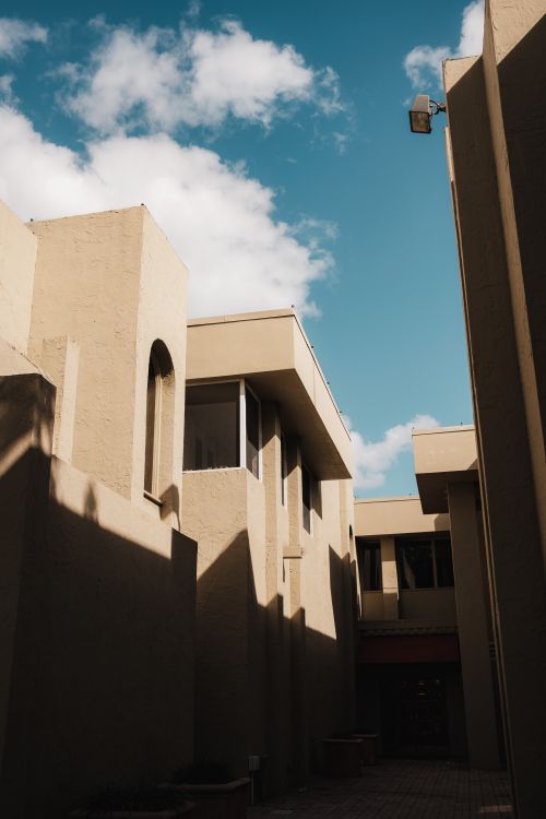Free A striking view of modern architecture with geometric forms casting shadows under a bright blue sky. Stock Photo