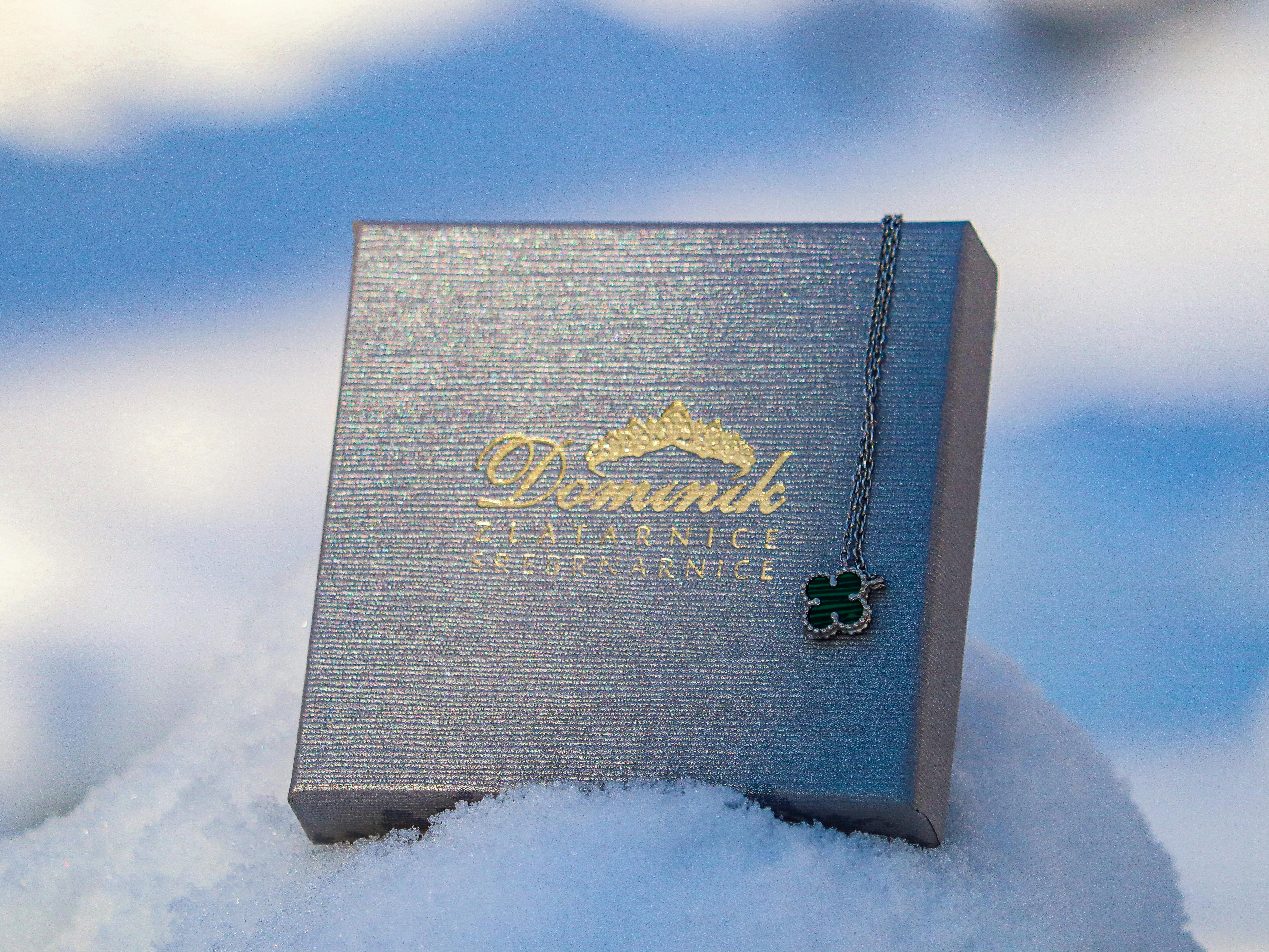 A stylish jewelry box with a necklace displayed outdoors on a snowy winter day.