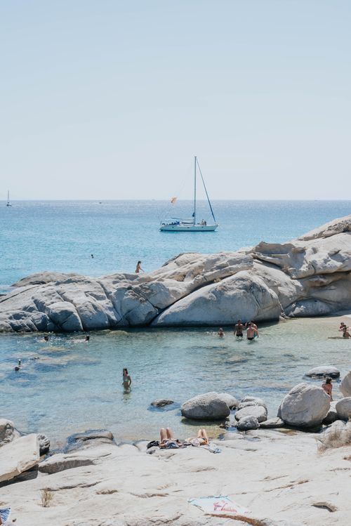 Free A peaceful beach scene with swimmers and a sailboat under the summer sun. Stock Photo