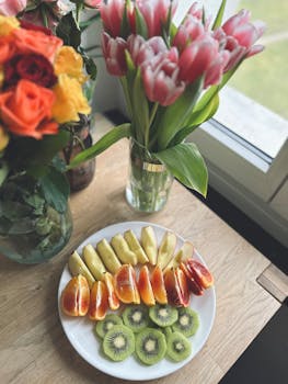 Fresh sliced fruit with vibrant floral arrangements by a window, evoking a cheerful indoor vibe.
