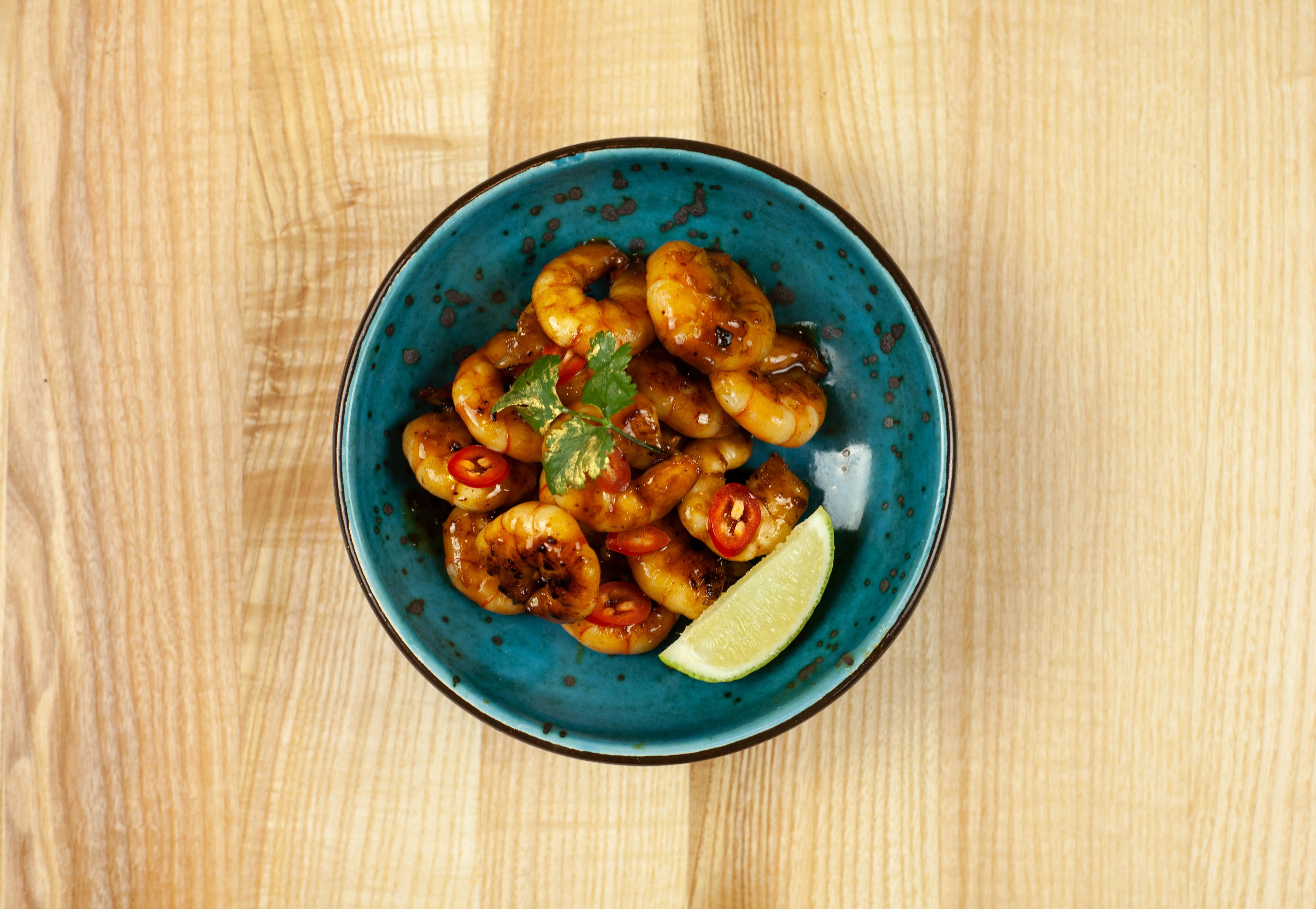 A generous bowl of creamy white grits topped with pink Gulf shrimp in a rich brown habanero sauce, garnished with sliced green onions and fresh parsley