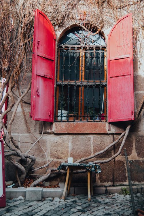 Free A rustic stone wall with open red shutters and overgrown vines creates an inviting and timeless scene. Stock Photo