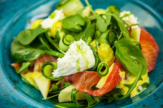 Delicious fresh salad with spinach, ricotta cheese, smoked salmon, cucumber, apple on a vibrant blue plate.