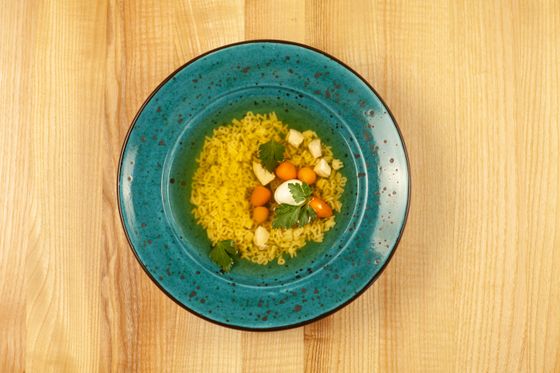 Clear golden broth with tiny pasta, carrot rounds, chicken pieces, egg and parsley in teal bowl