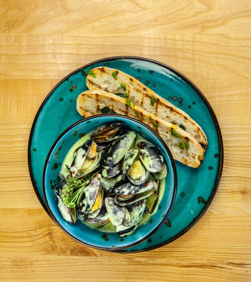 Free Top view of creamy mussels with grilled bread on a vibrant blue plate, perfect for seafood lovers. Stock Photo