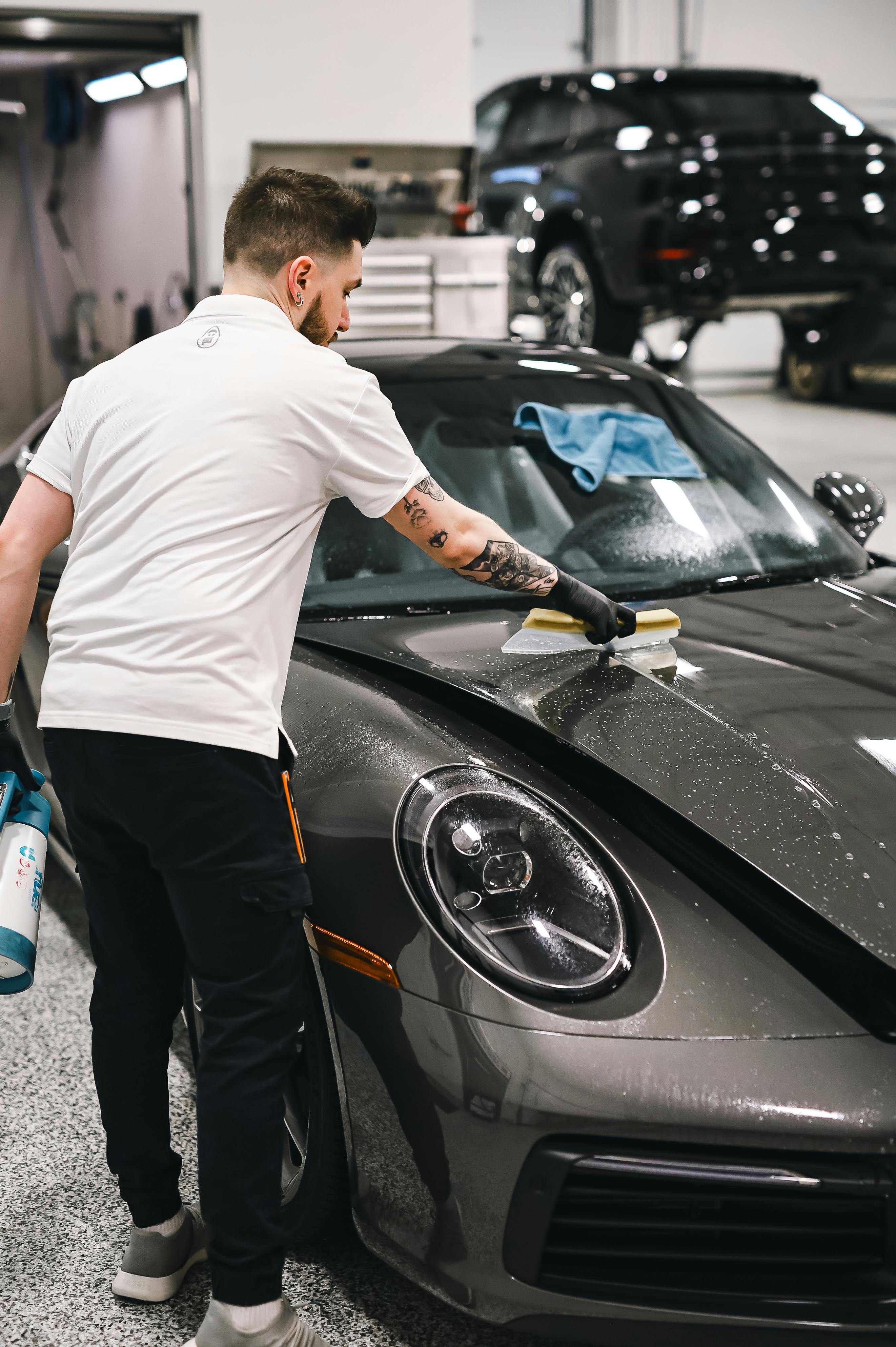 A man is cleaning a car with a sponge in a garage.