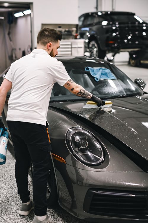 Free Man professionally detailing a black sports car hood in a modern garage. Stock Photo