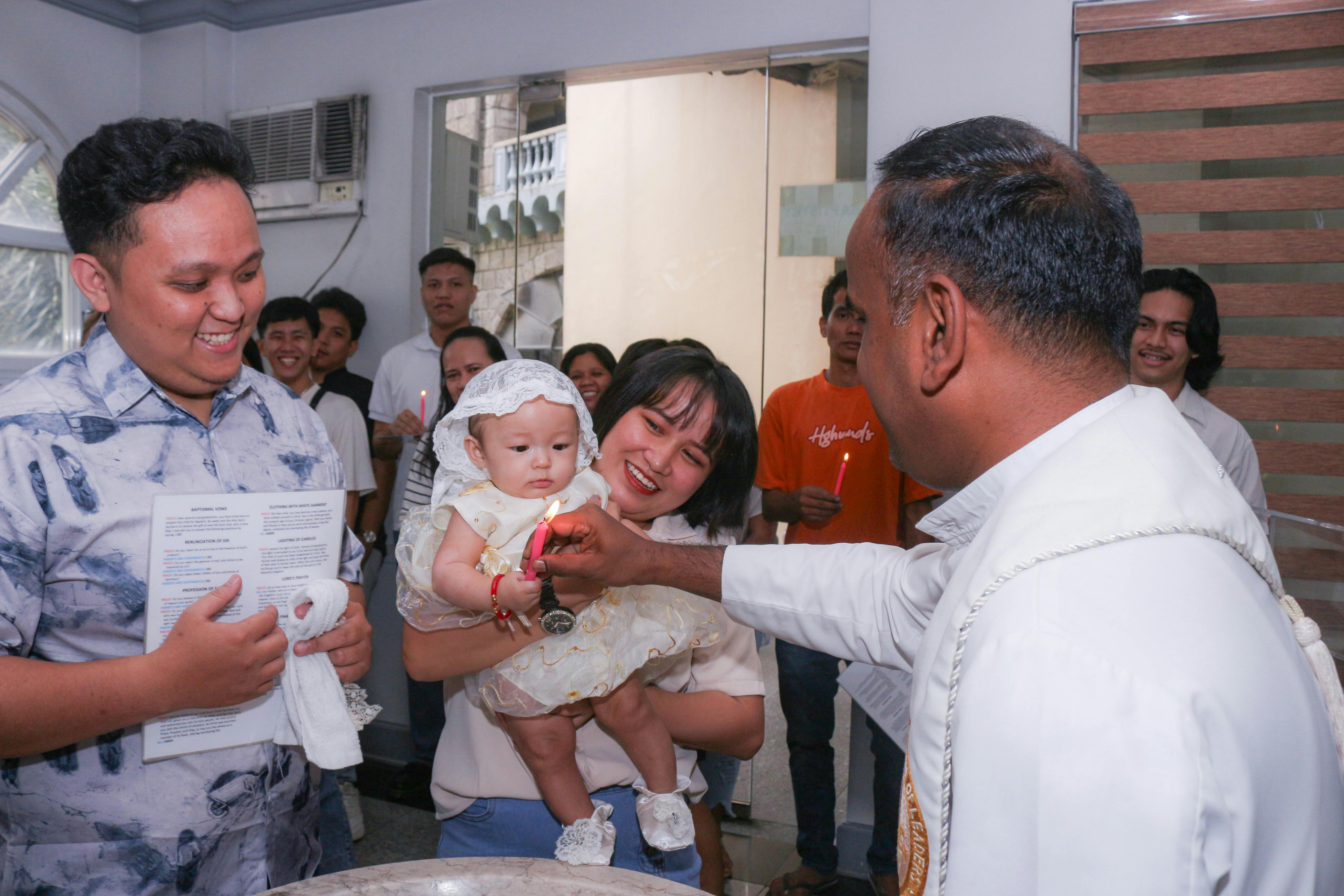 A joyful family celebrating a baby's baptism ceremony in a church setting with a priest.