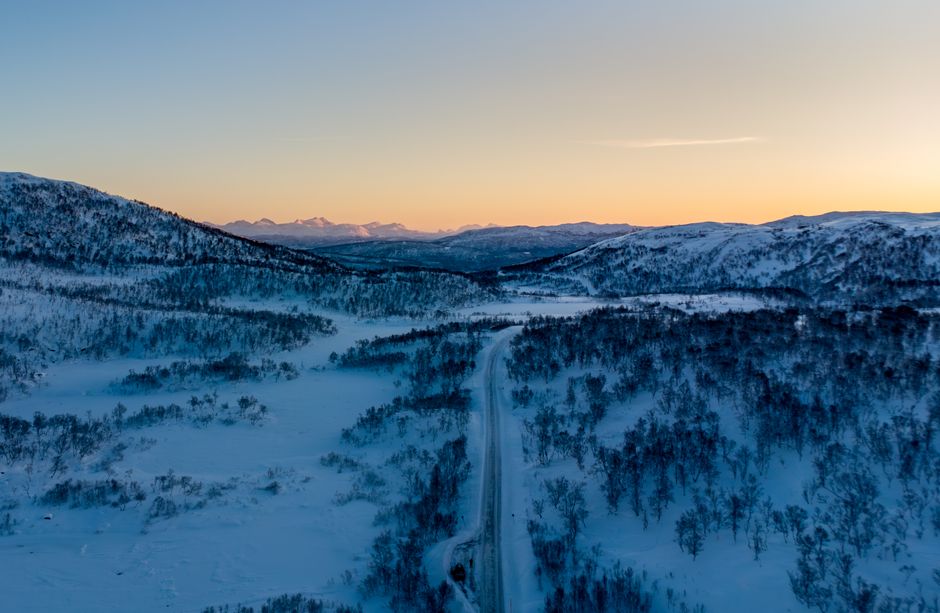 A breathtaking aerial view of Harstad's snowy landscape and mountains at sunset.