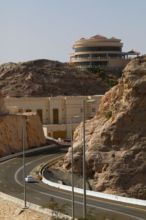 Free A winding road through Jabal Hafeet with stunning rock formations and a distant architectural landmark. Stock Photo