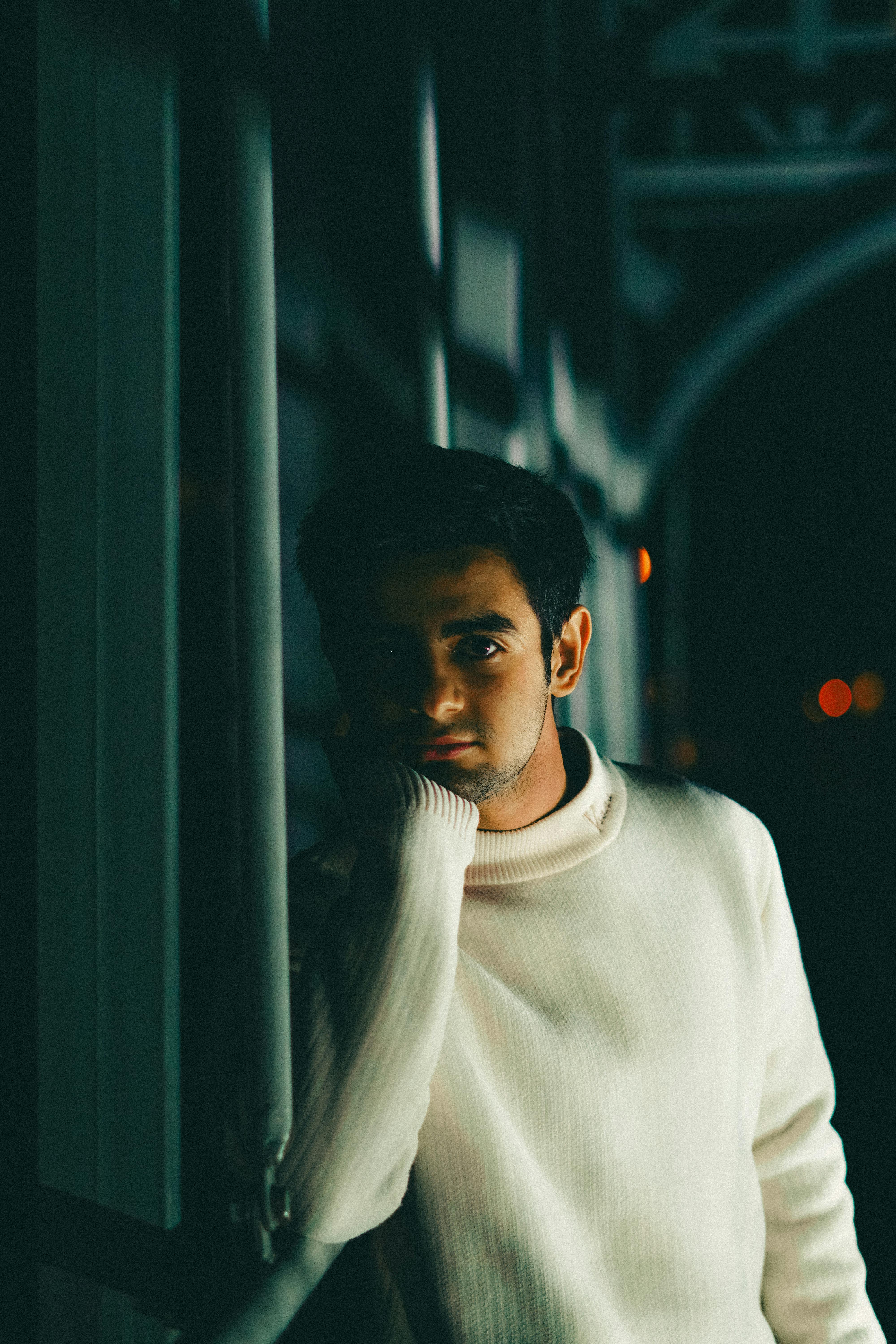 Artistic shot of a man in a white sweater posing indoors with thoughtful expression.