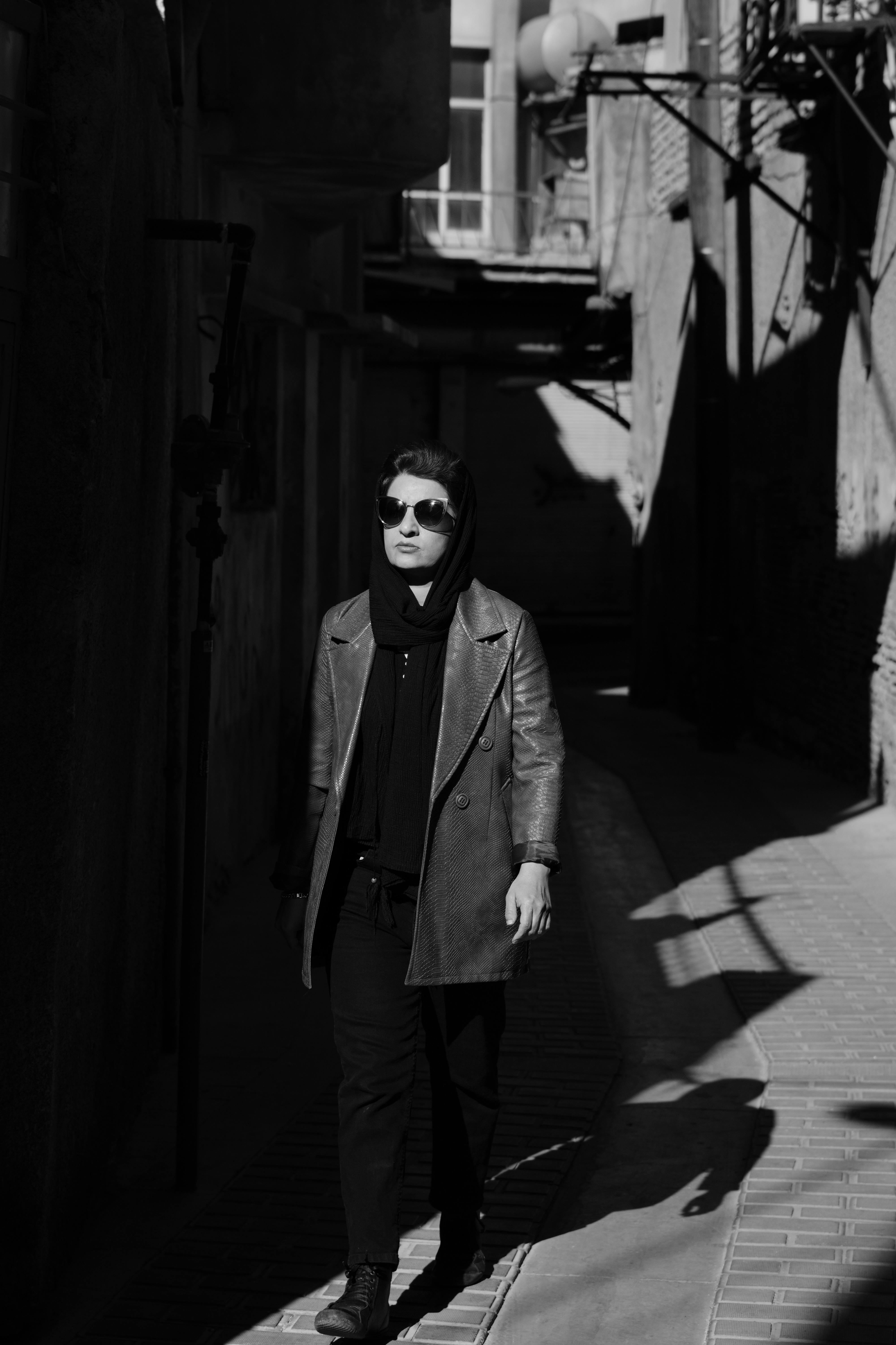 Fashionable individual walking through city alley in striking black and white photography.