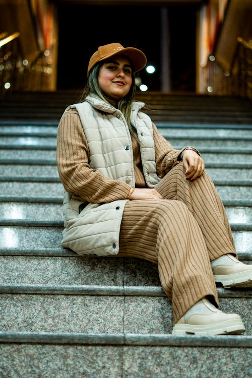 Woman in Cap and Vest Sitting on Stairs