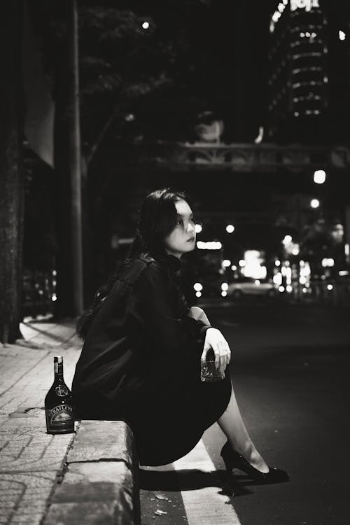 Woman Sitting with Bottle by Street