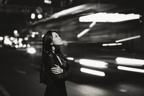 Bus Passing by Woman Standing on Street at Night