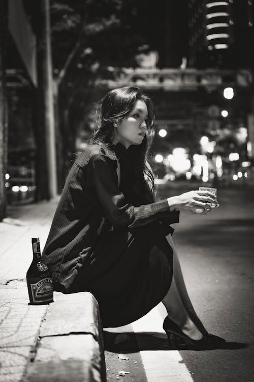 Woman Sitting with Glass on Street at Night