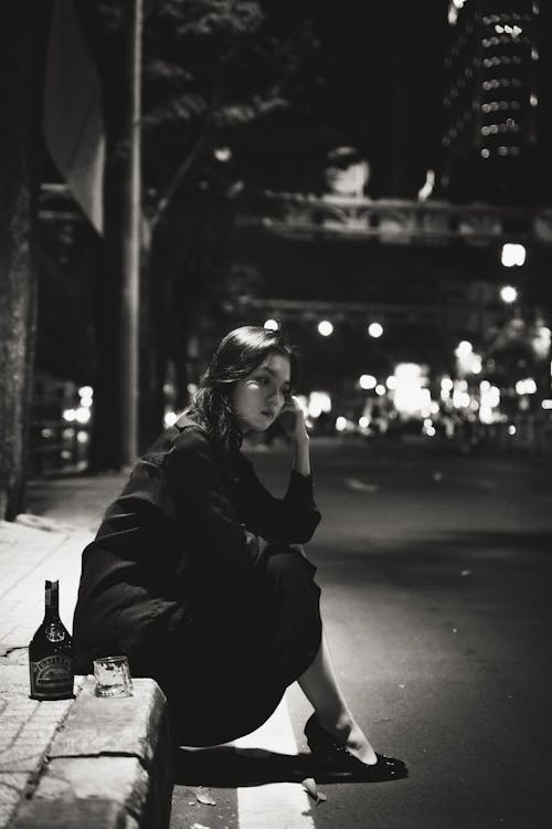 Woman Sitting by Street with Bottle and Glass and Thinking