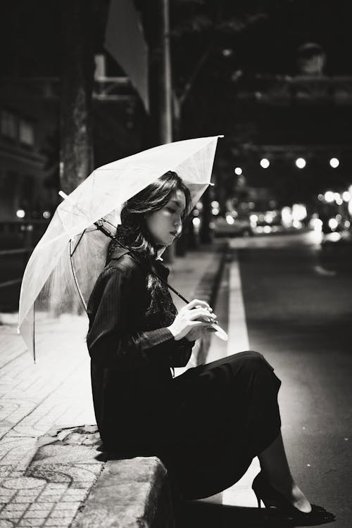 Woman Sitting with Umbrella by Street at Night