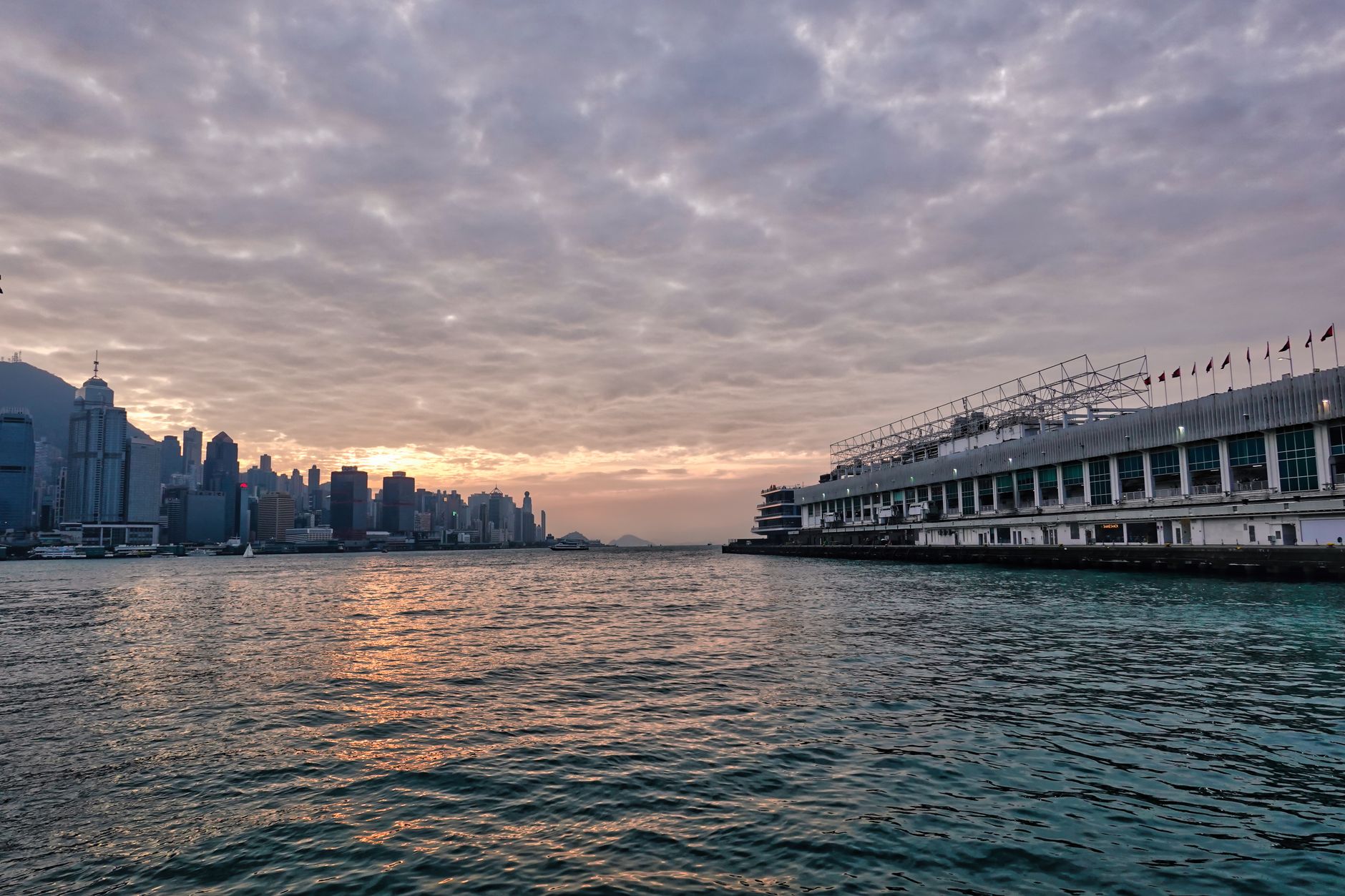 Scenic view of Kowloon harbor with cityscape and dramatic sunset sky in Hong Kong.