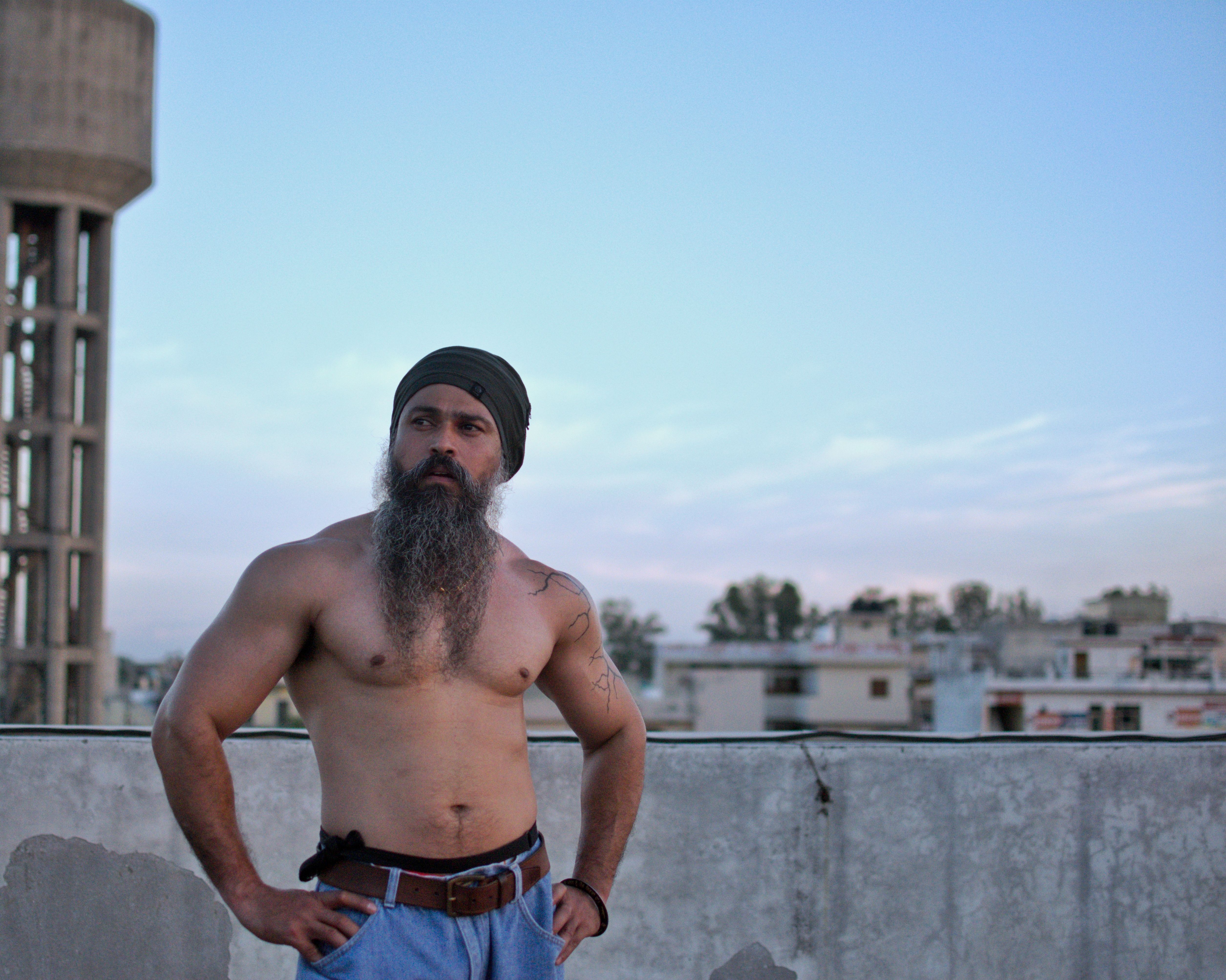 Portrait of a topless bearded man standing confidently on an urban rooftop in PB, India.